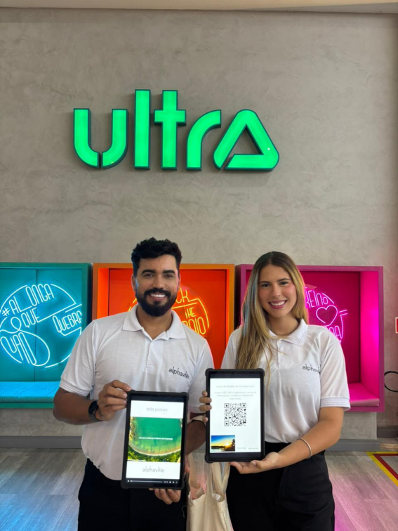 Equipe da UNNA apresentando tablets com conteúdo digital em evento da marca Ultra, com neon colorido ao fundo.